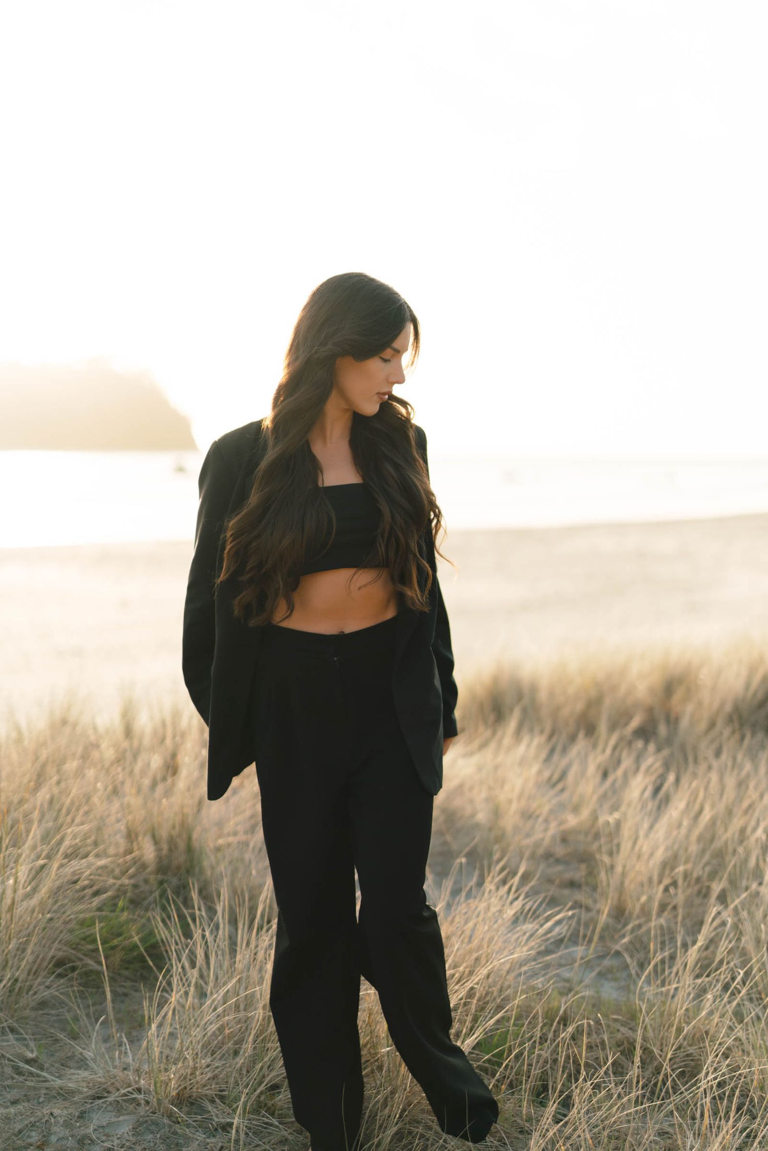 A figure in a black outfit poses in a field of tall grass during golden hour.
