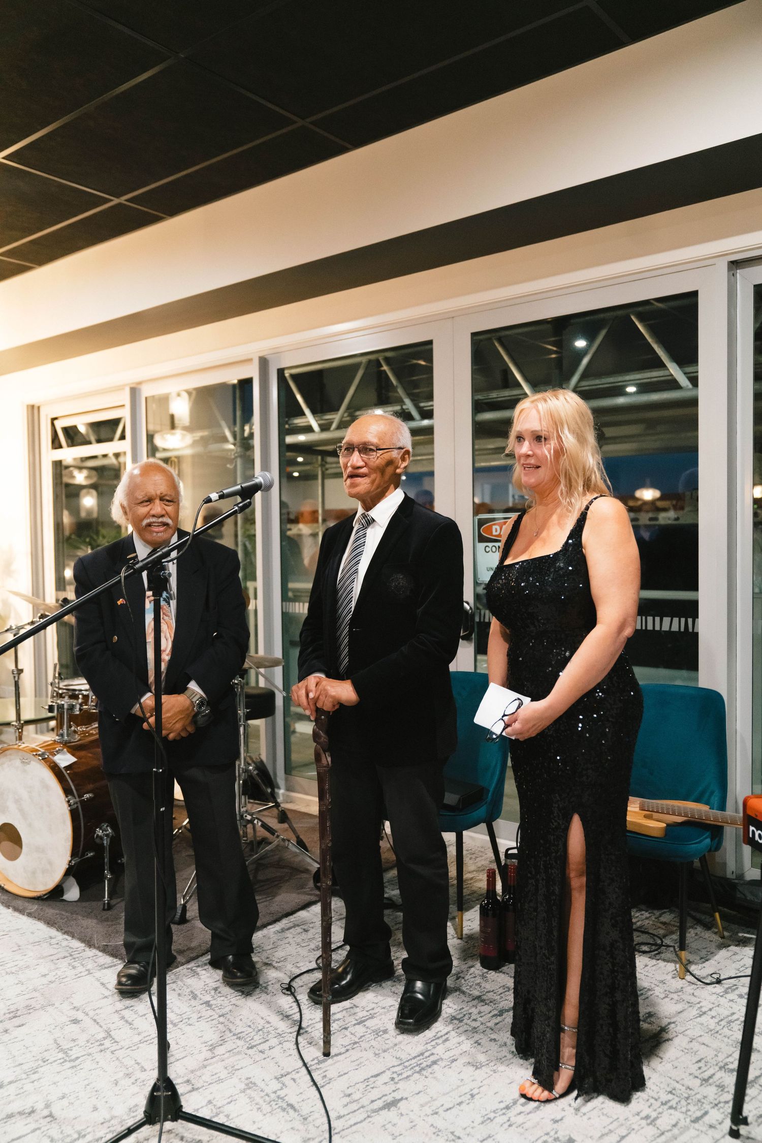 Three performers standing at microphones on stage during an evening event.