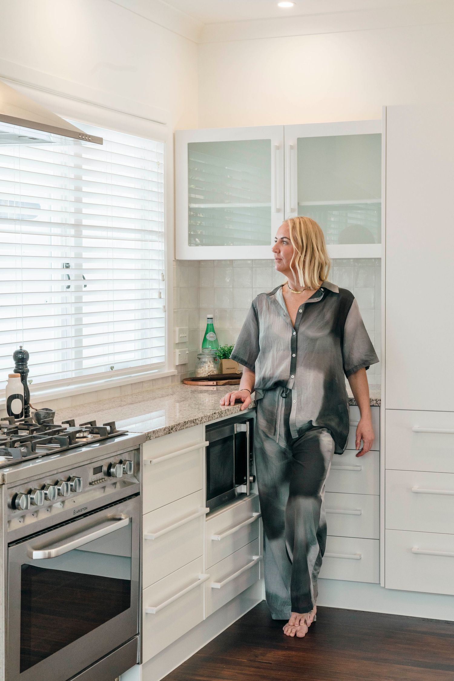Modern white kitchen with sleek cabinetry, gas stovetop, and large windows filtered with white blinds.