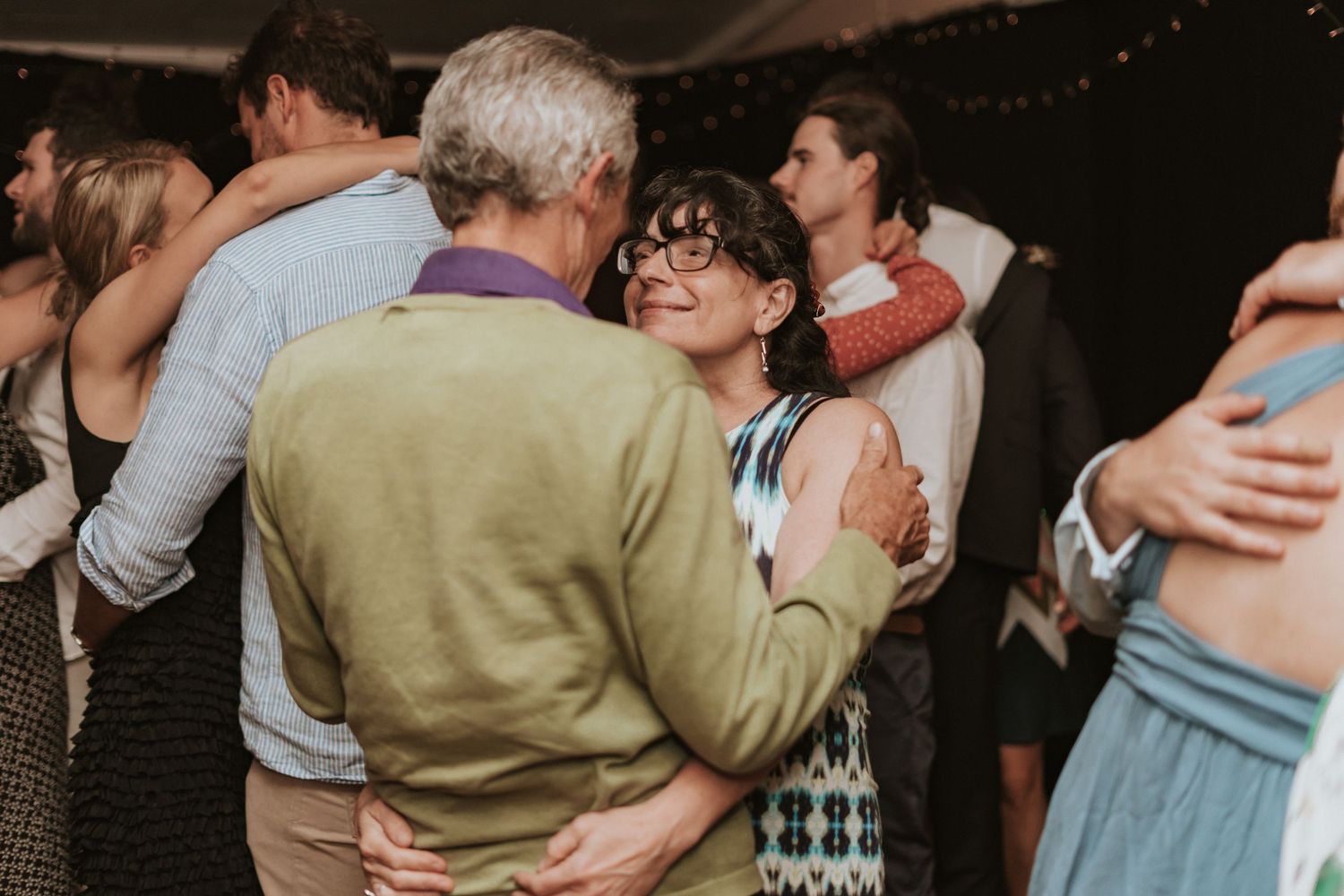 People dancing and embracing at a dimly lit party or celebration venue with romantic mood lighting.