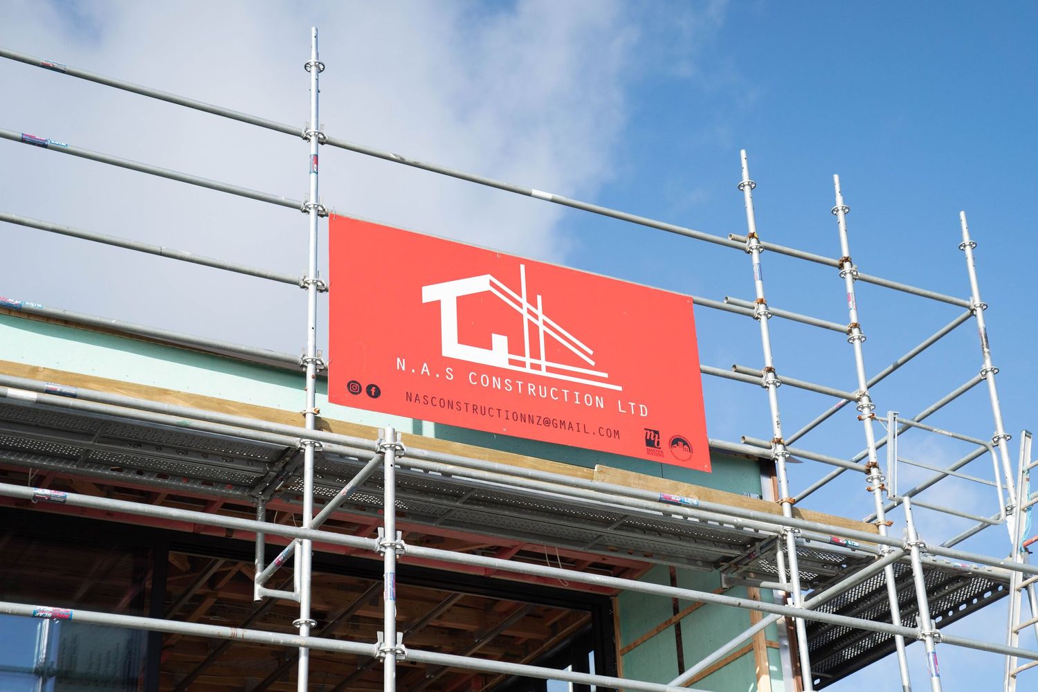 Construction site scaffolding installed on building exterior with red banner signage visible against blue sky.