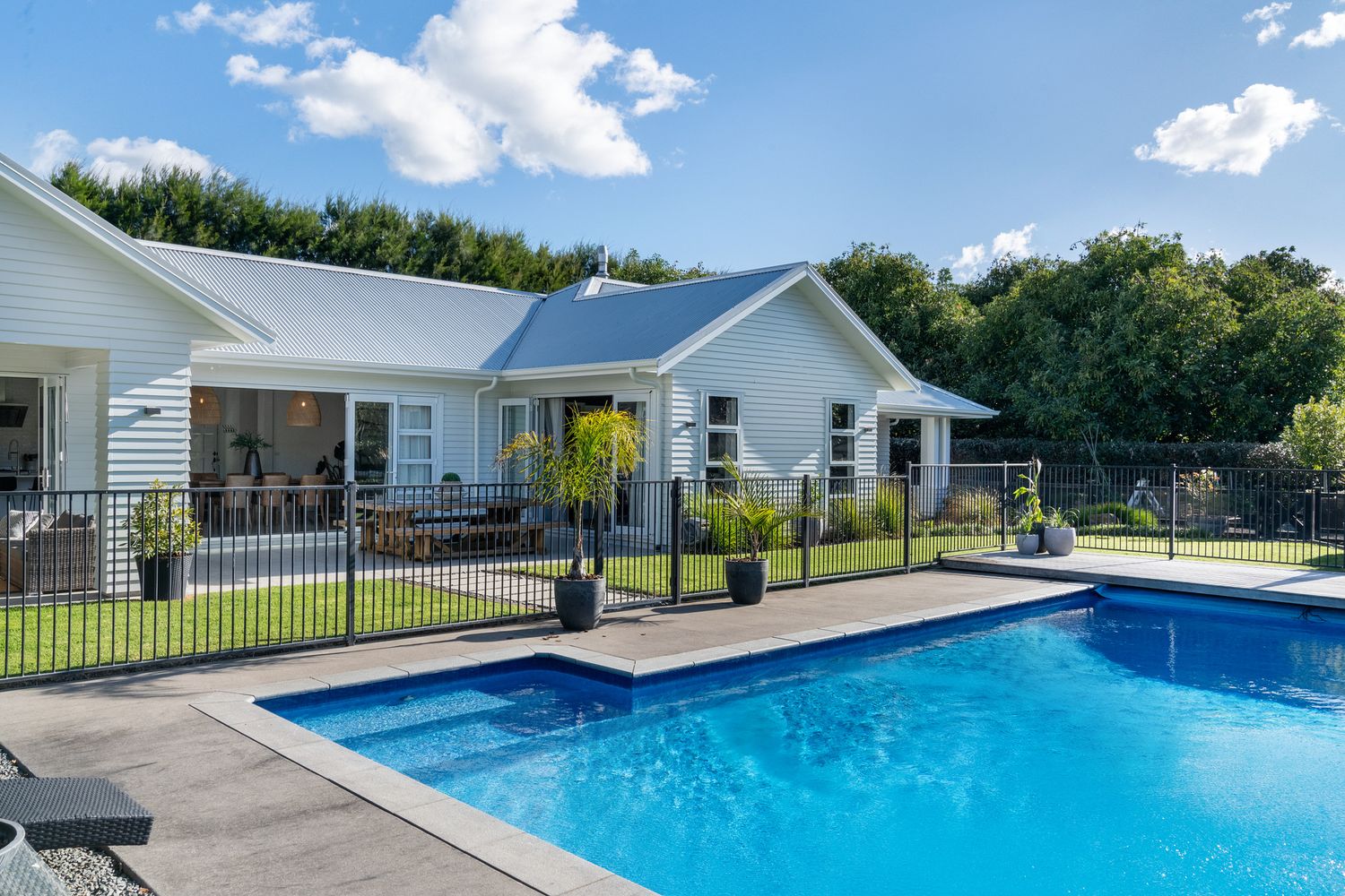 Modern home exterior with fenced swimming pool and white cladding on a sunny day.