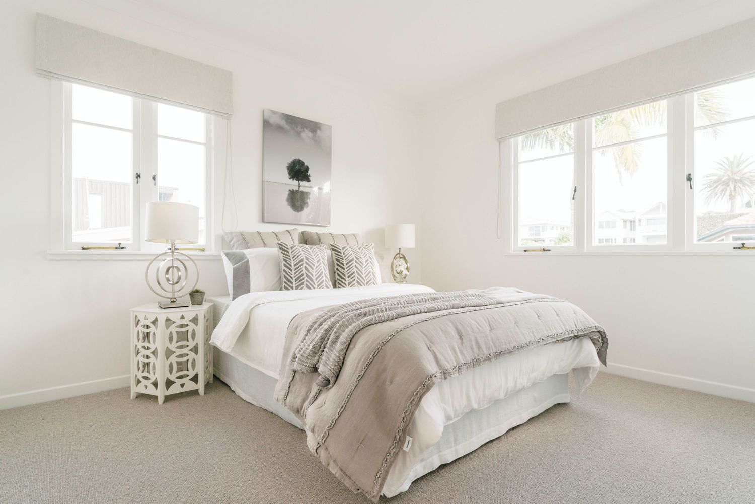 Airy white bedroom with beige accents, multiple windows, and decorative side tables.