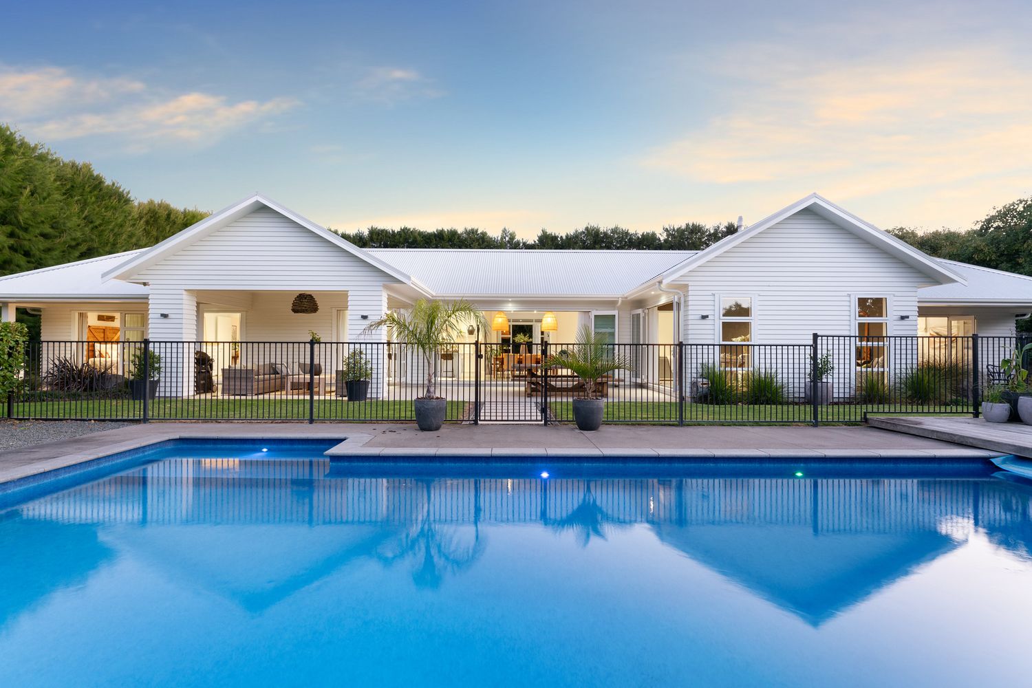 Elegant white house with swimming pool and decorative iron fencing at dusk.