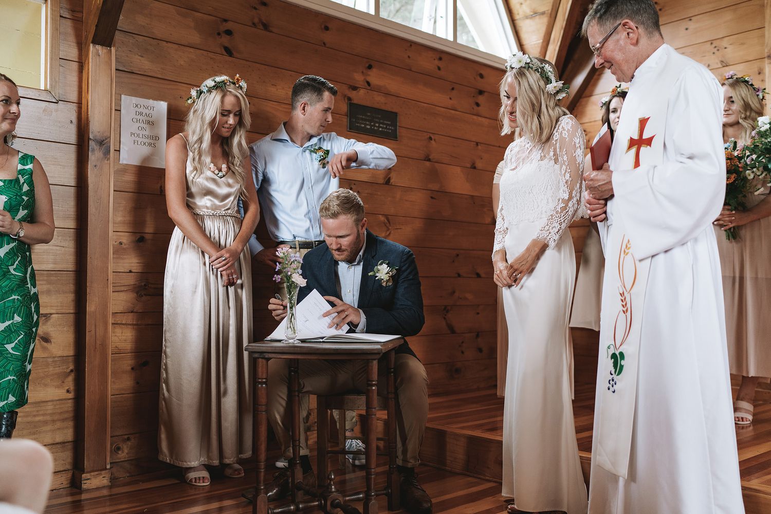 A small wedding ceremony takes place inside a rustic wooden cabin as people gather around someone signing documents.