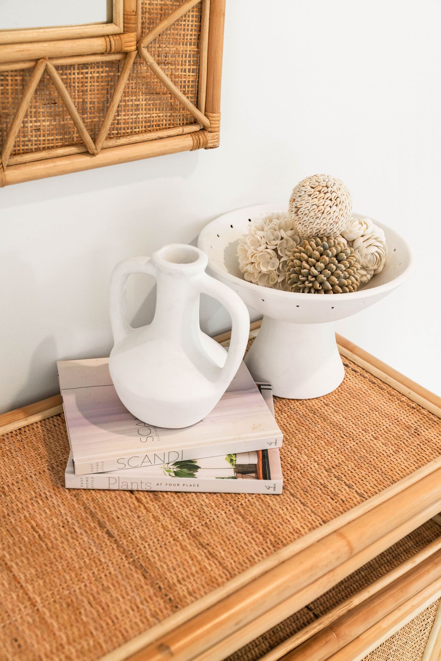White ceramic vase and decorative spheres displayed on rattan furniture with a magazine and wooden wall art.