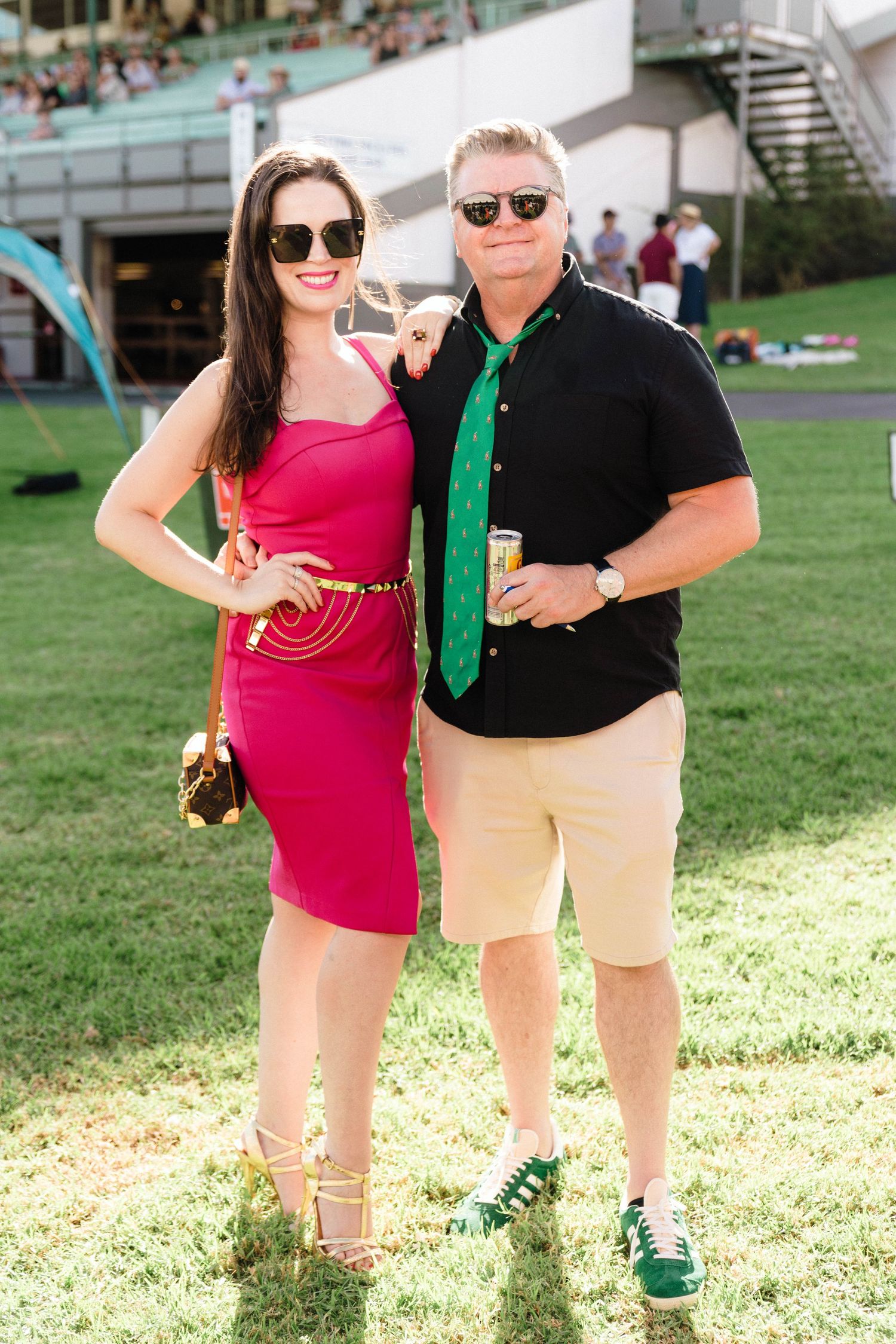 Couple poses outdoors on sunny lawn, wearing contrasting red and black outfits with sunglasses.