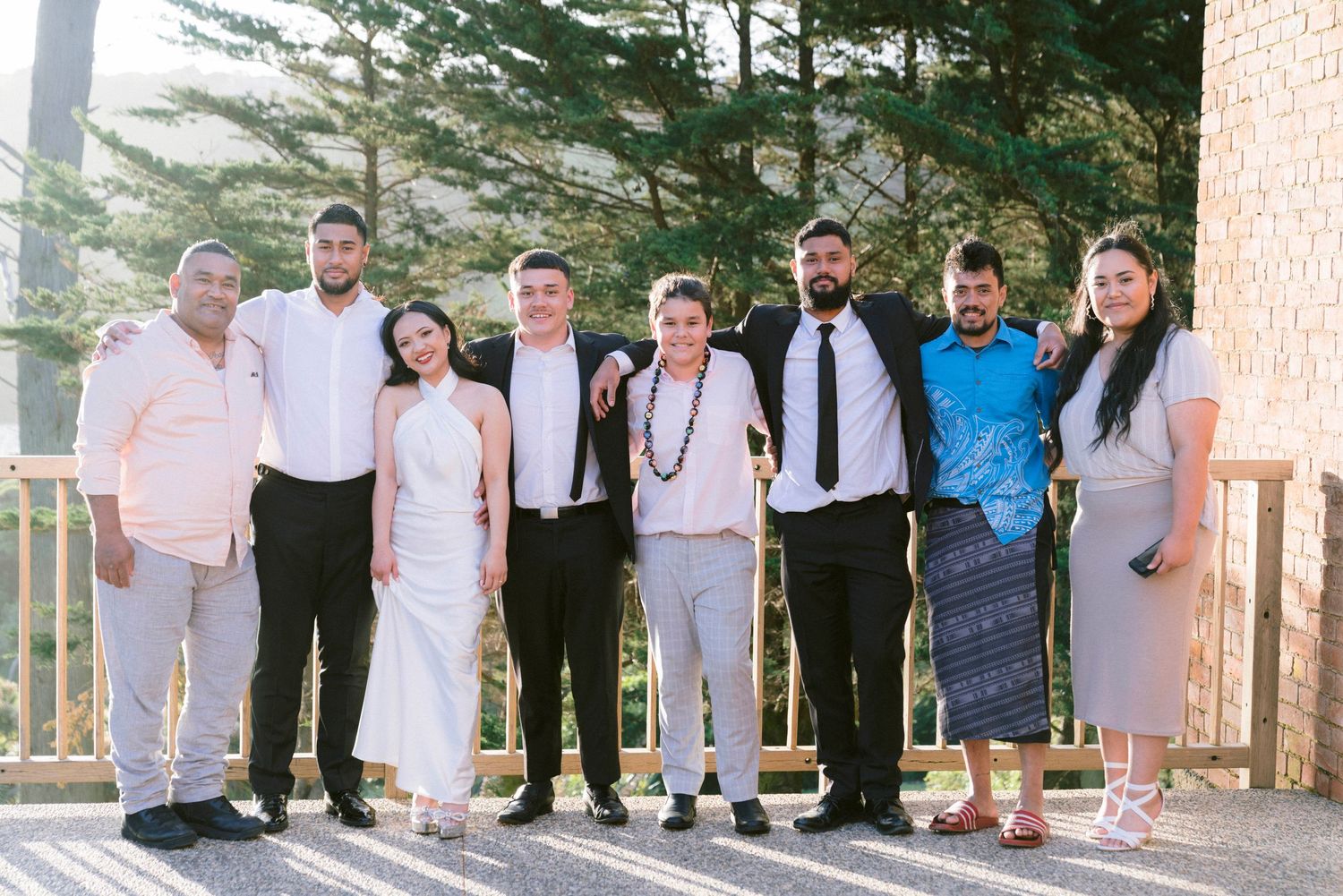 Wedding party members lined up against a brick wall for a group photo.
