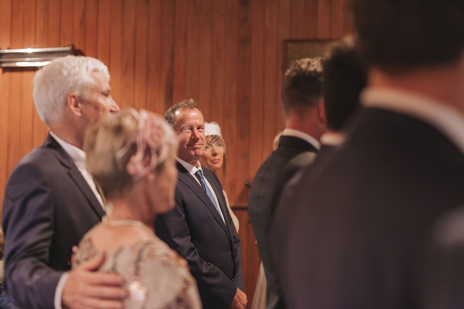 A group of formally dressed people engaged in conversation in a wood-paneled room at an event.