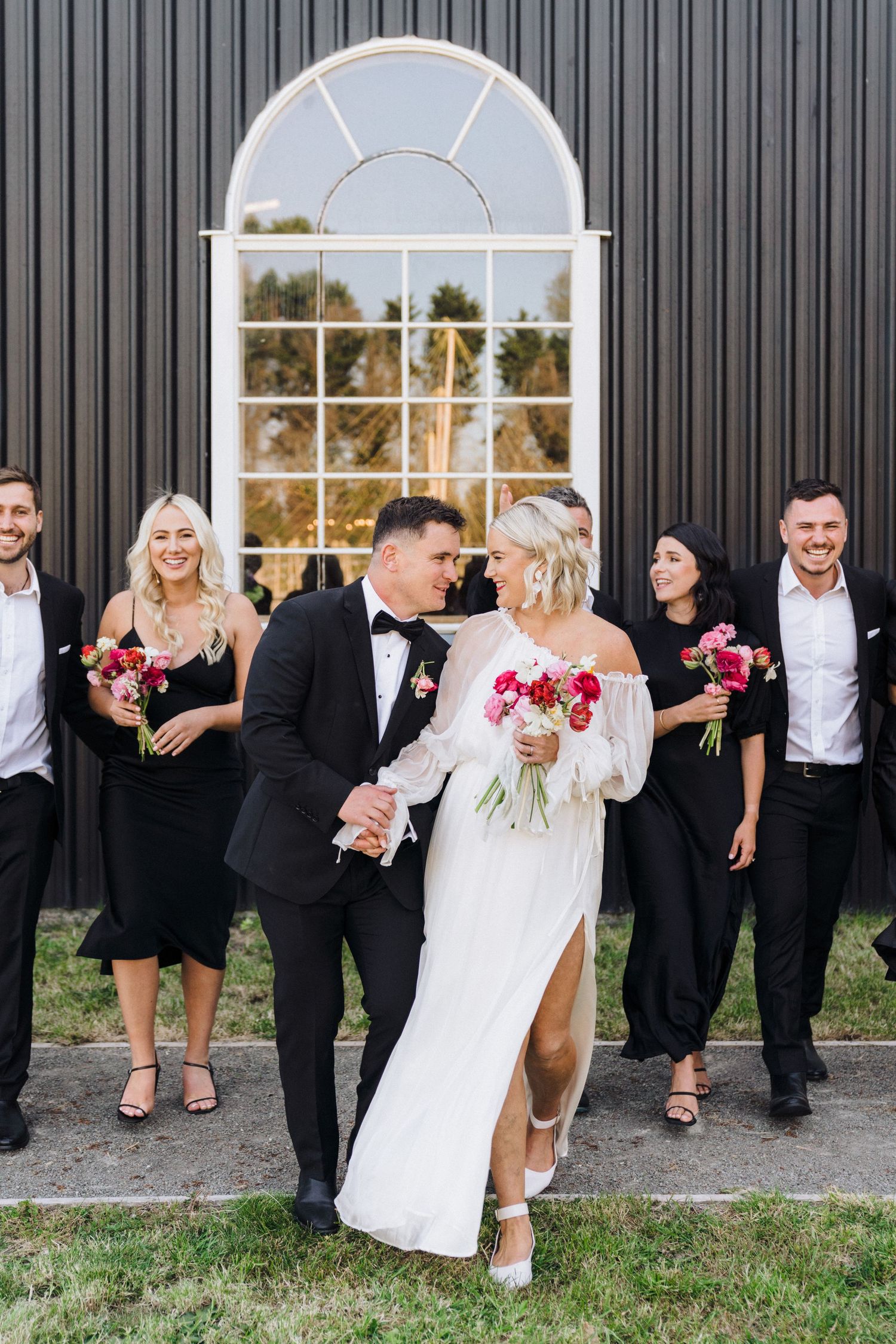 A bridal party poses in front of a modern black building with an arched window.