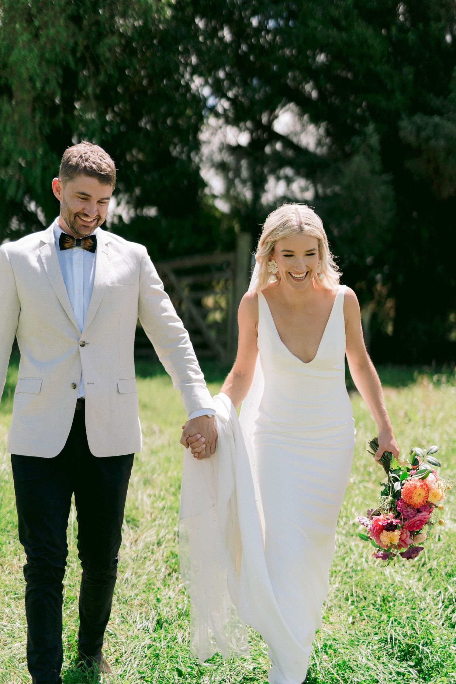 A joyful couple walking outdoors in wedding attire with eucalyptus trees in the background.