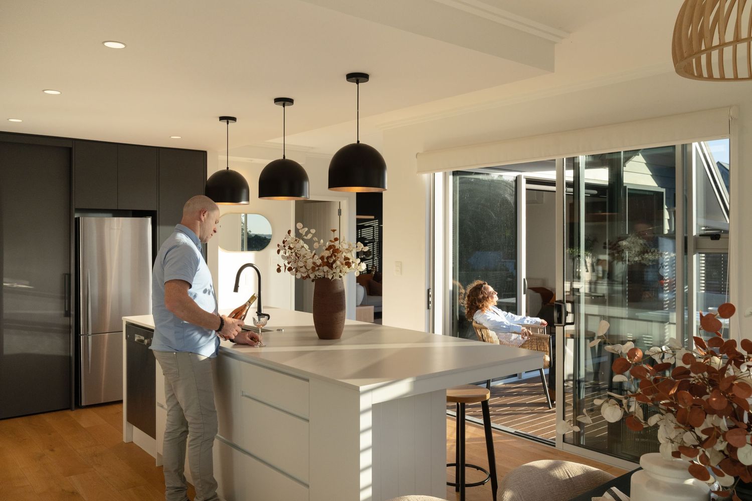Modern open-plan kitchen with island bench, pendant lights, and sliding doors leading to outdoor living area.