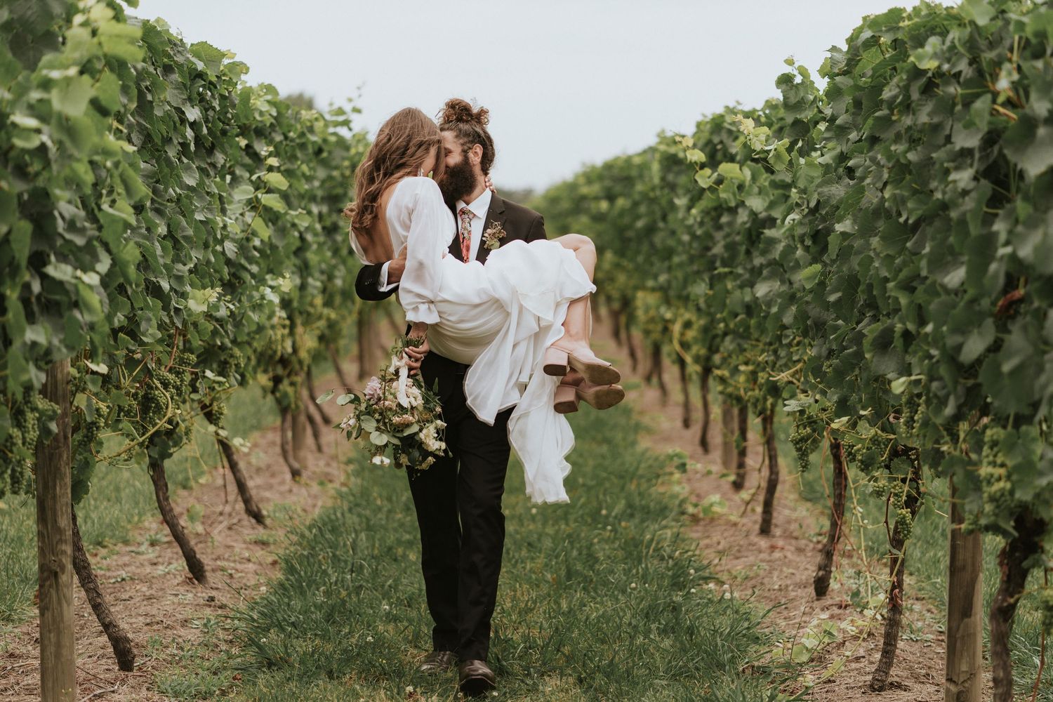 Romantic couple walking through scenic vineyard rows during golden hour at a countryside winery.