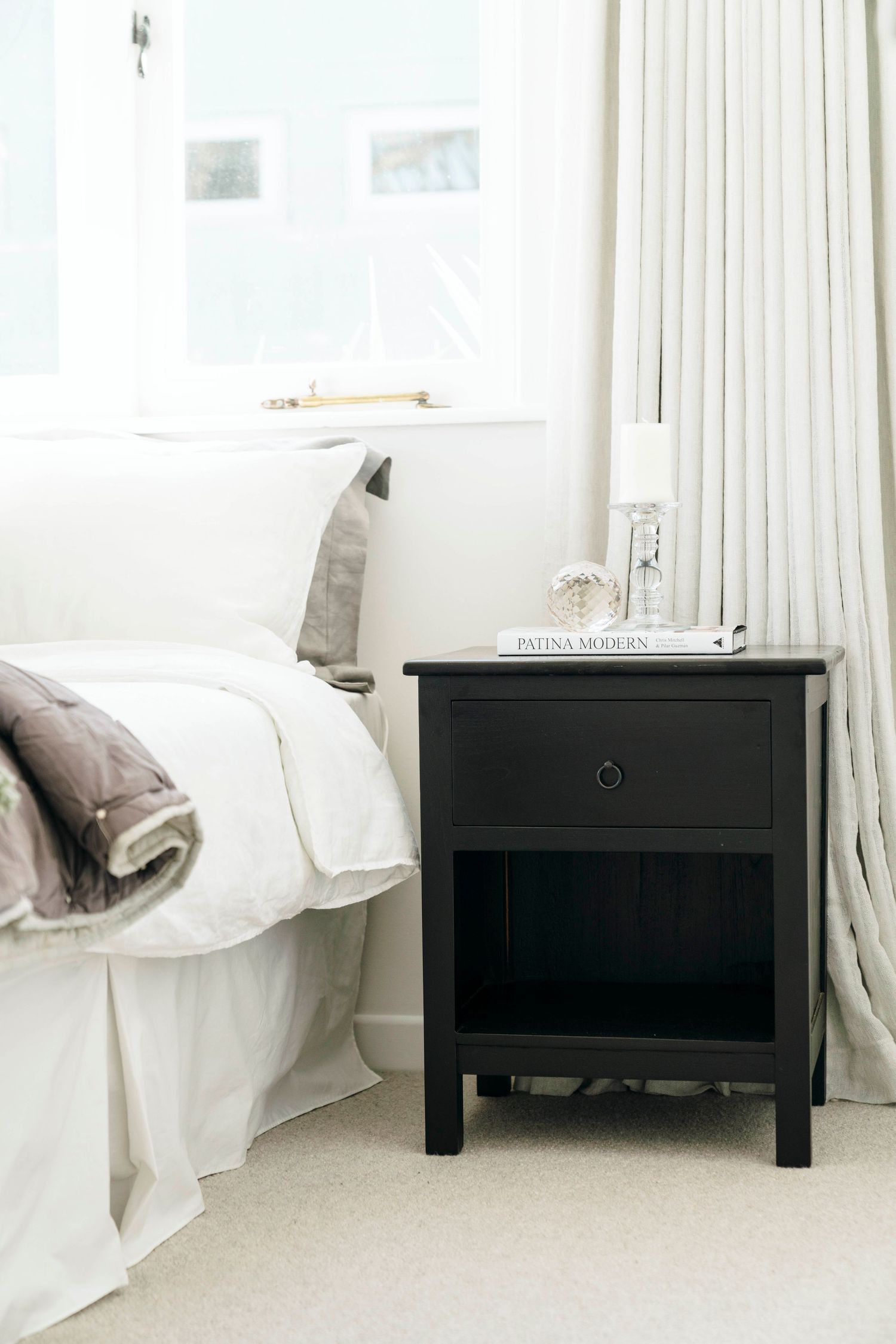 Black wooden bedside tables with drawers positioned against a white wall with flowing curtains.