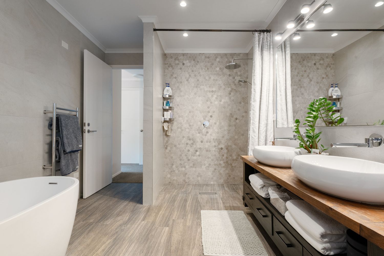 Luxurious bathroom featuring wooden vanity, vessel sink and marble-look shower wall.