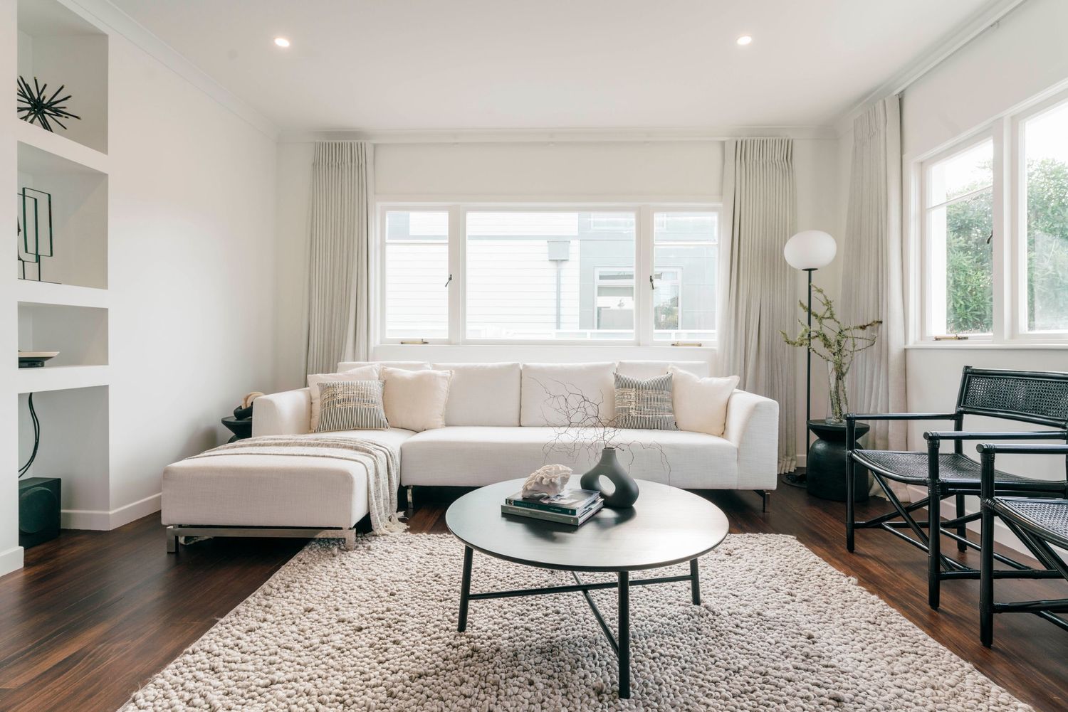 Contemporary living room with white sectional sofa, round coffee table, and plush area rug on dark hardwood floors.