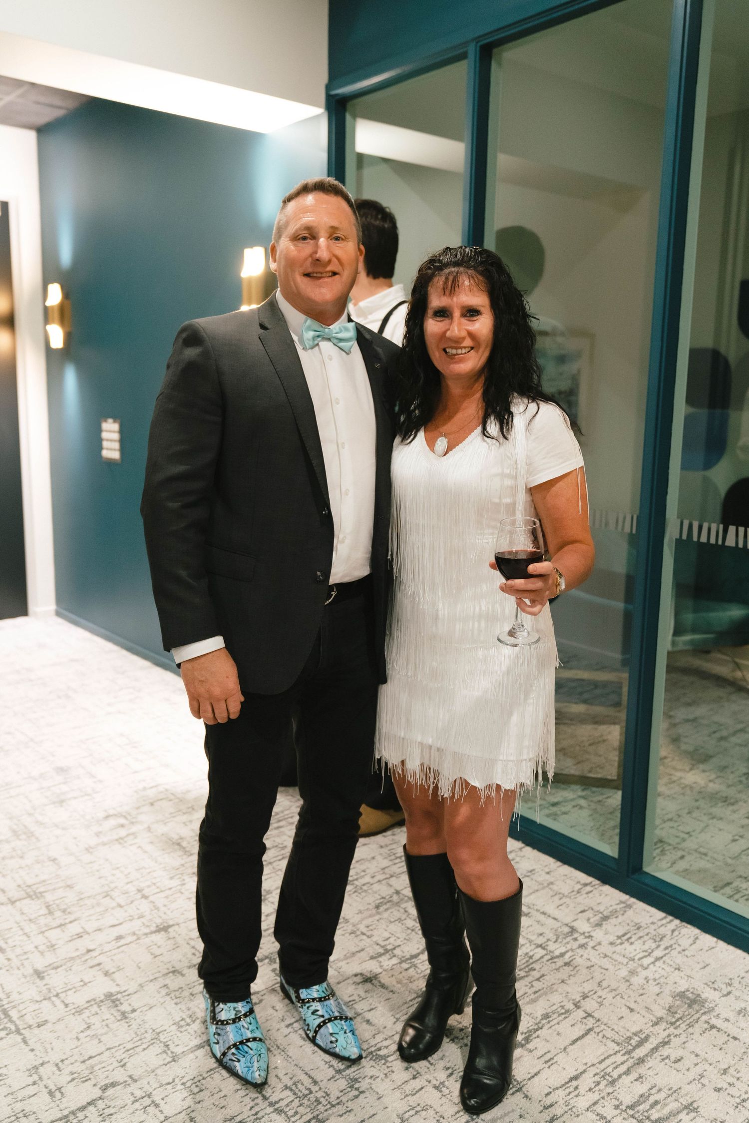 A couple dressed in black and white formal attire pose together at an indoor event space.