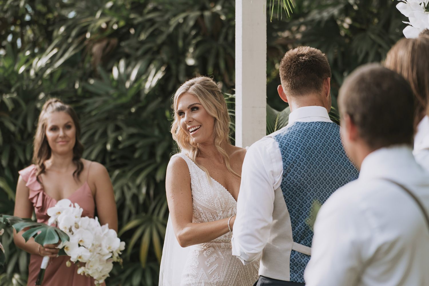 Wedding guests mingle and celebrate at an outdoor venue surrounded by tropical foliage.