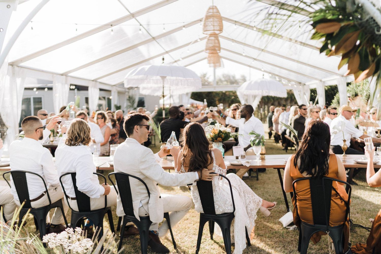Wedding reception under elegant white tent canopy with lantern decorations and rustic outdoor dining setup.