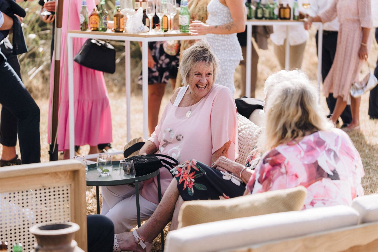 Wedding guests relaxing on pink chairs at outdoor reception venue.