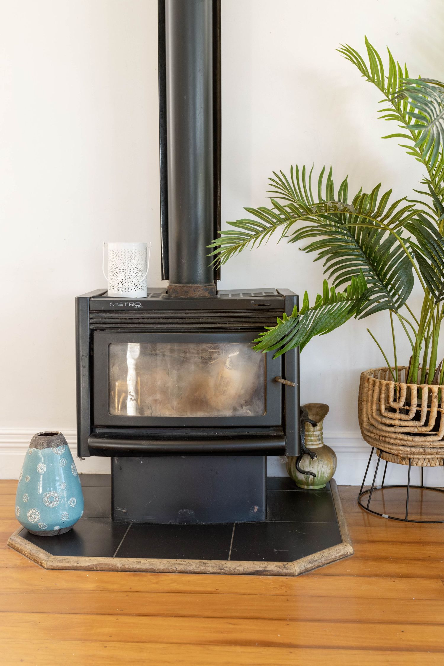 Black wood-burning stove with glass door surrounded by decorative plants and blue vase.