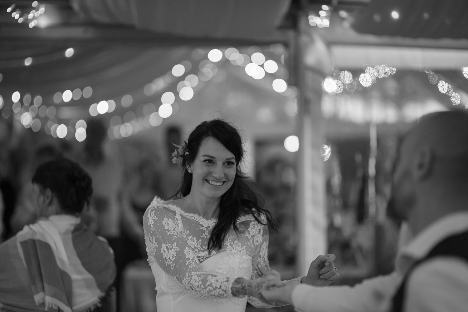 Wedding guests dance and celebrate together during a festive evening reception with glowing lights in the background.