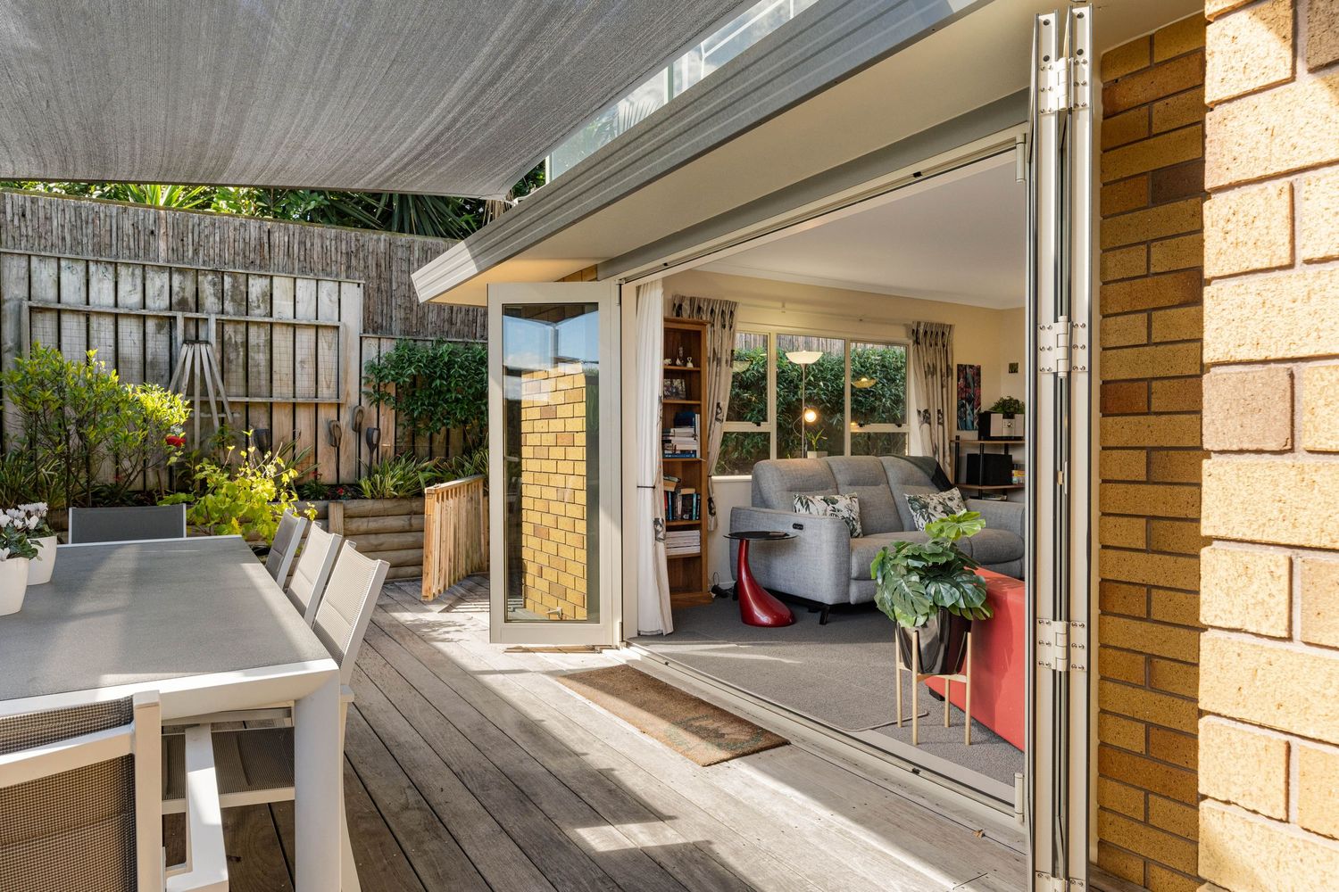 Modern outdoor patio with folding glass doors connecting to interior living space featuring wooden decking and stone accents.