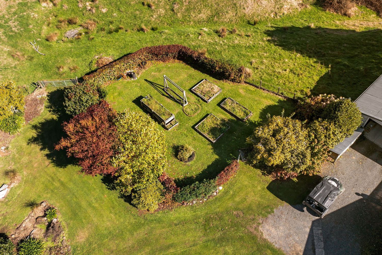 Aerial view of a structured garden with geometric raised beds on green hillside property.