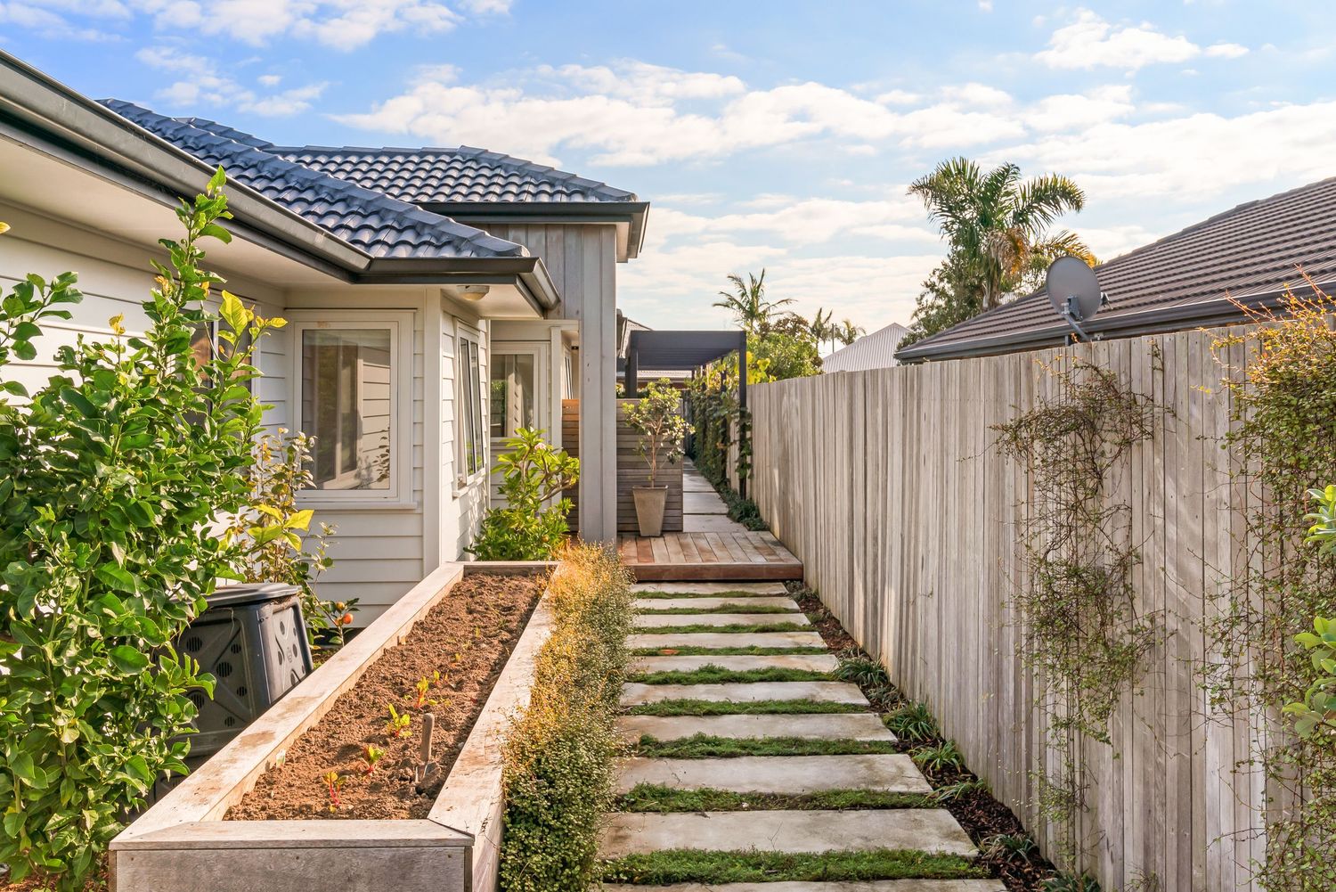Contemporary home garden path with stepping stones and raised planter bed along wooden fence.