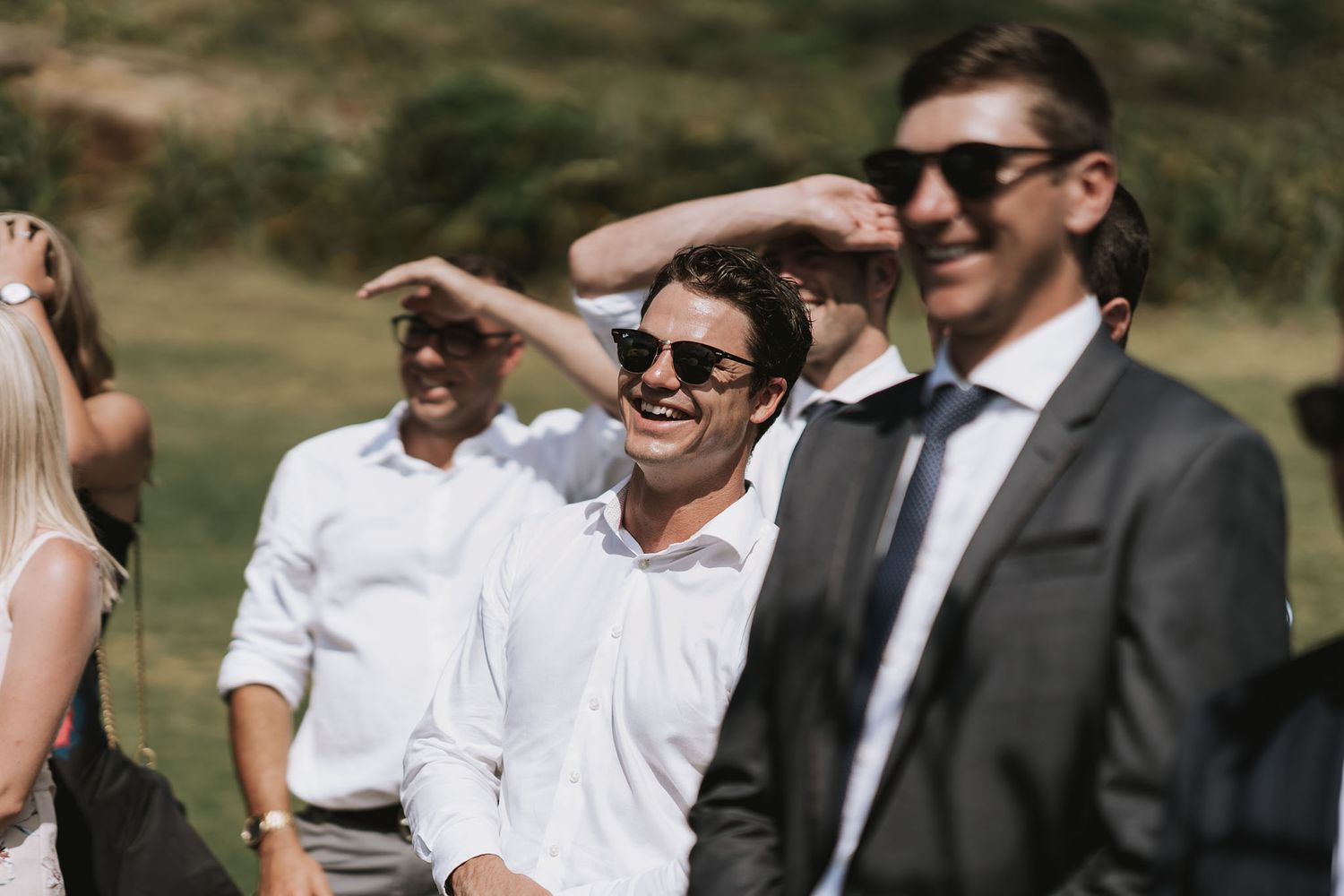 Group of people dressed formally in suits and white shirts gathered outdoors in bright natural lighting.