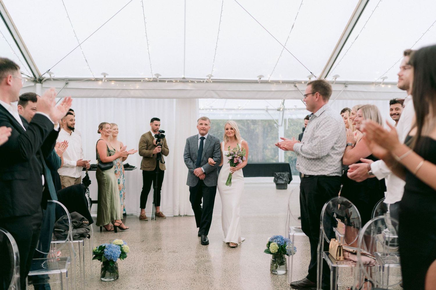 Wedding guests dance and celebrate together under a white tent with string lights overhead.