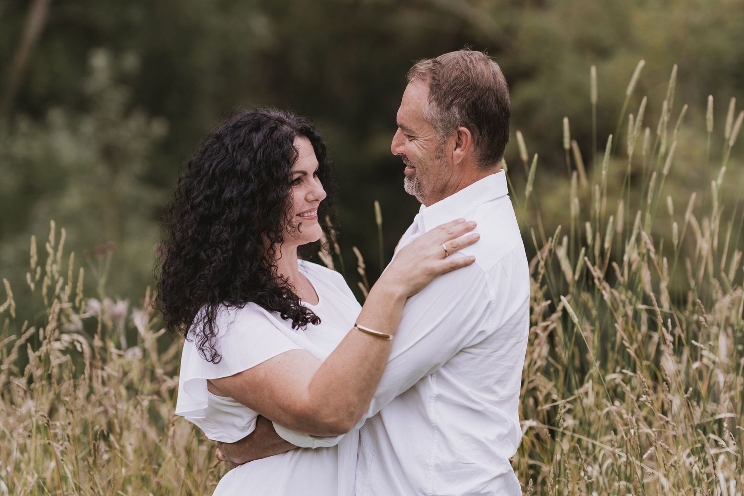 A couple wearing white embraces in a golden field of tall grass during an outdoor photo session.