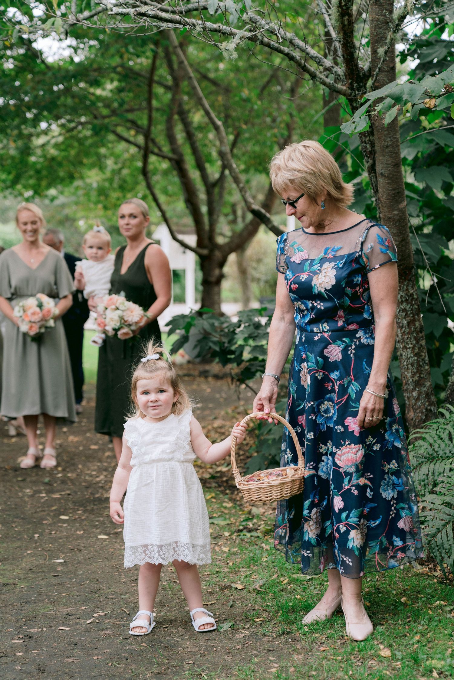 Flower girl in white dress walking down garden path during wedding ceremony.