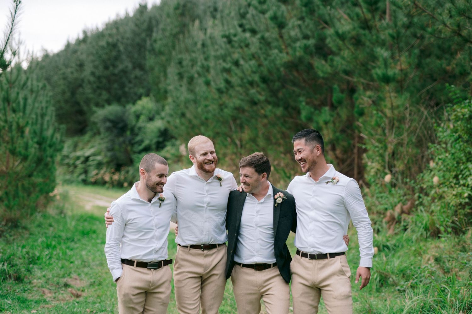 Groomsmen in light colored suits and dress shirts laughing together outdoors.