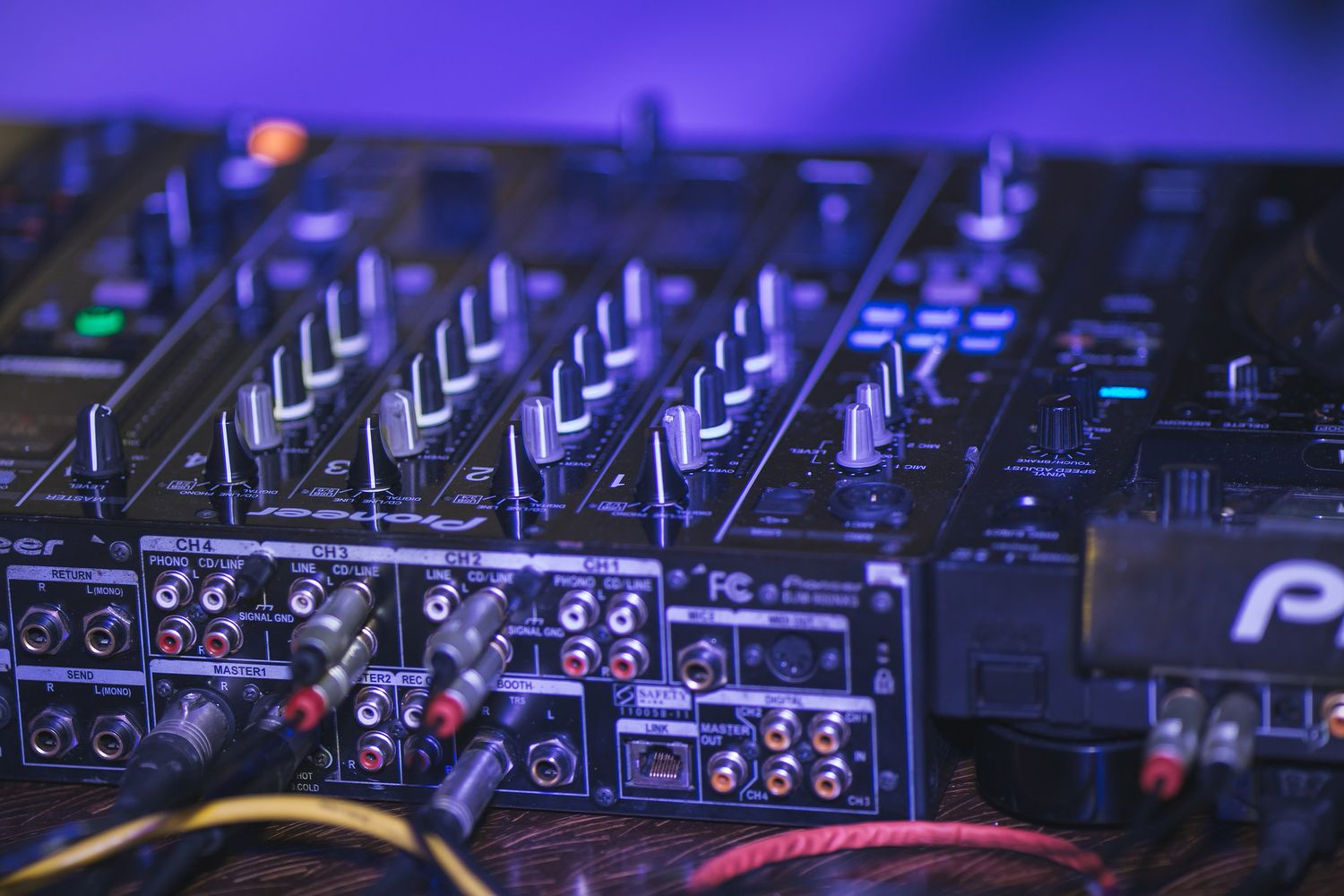 Close-up shot of a professional DJ mixer with knobs and faders illuminated by blue lighting.