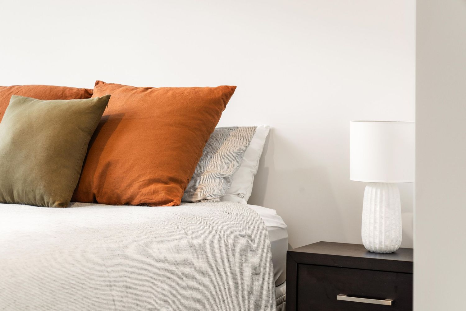 Minimalist white bedroom with plush bedding, orange accent pillows, and modern table lamps.