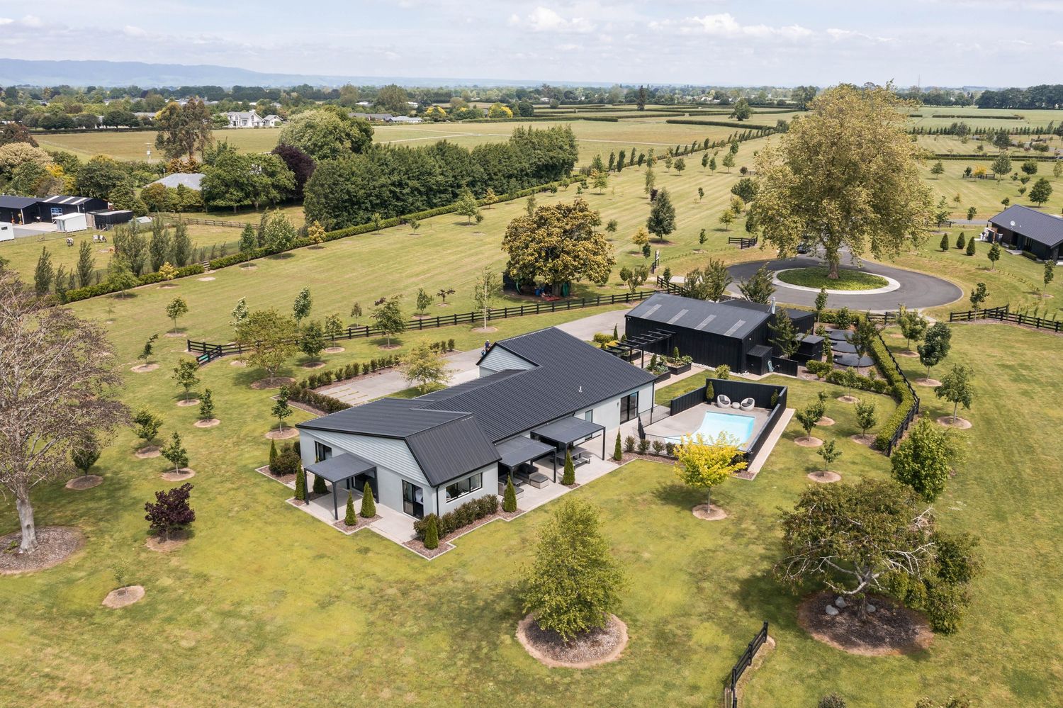 Modern country estate featuring a grey-roofed residence with manicured grounds and circular driveway in rural setting.