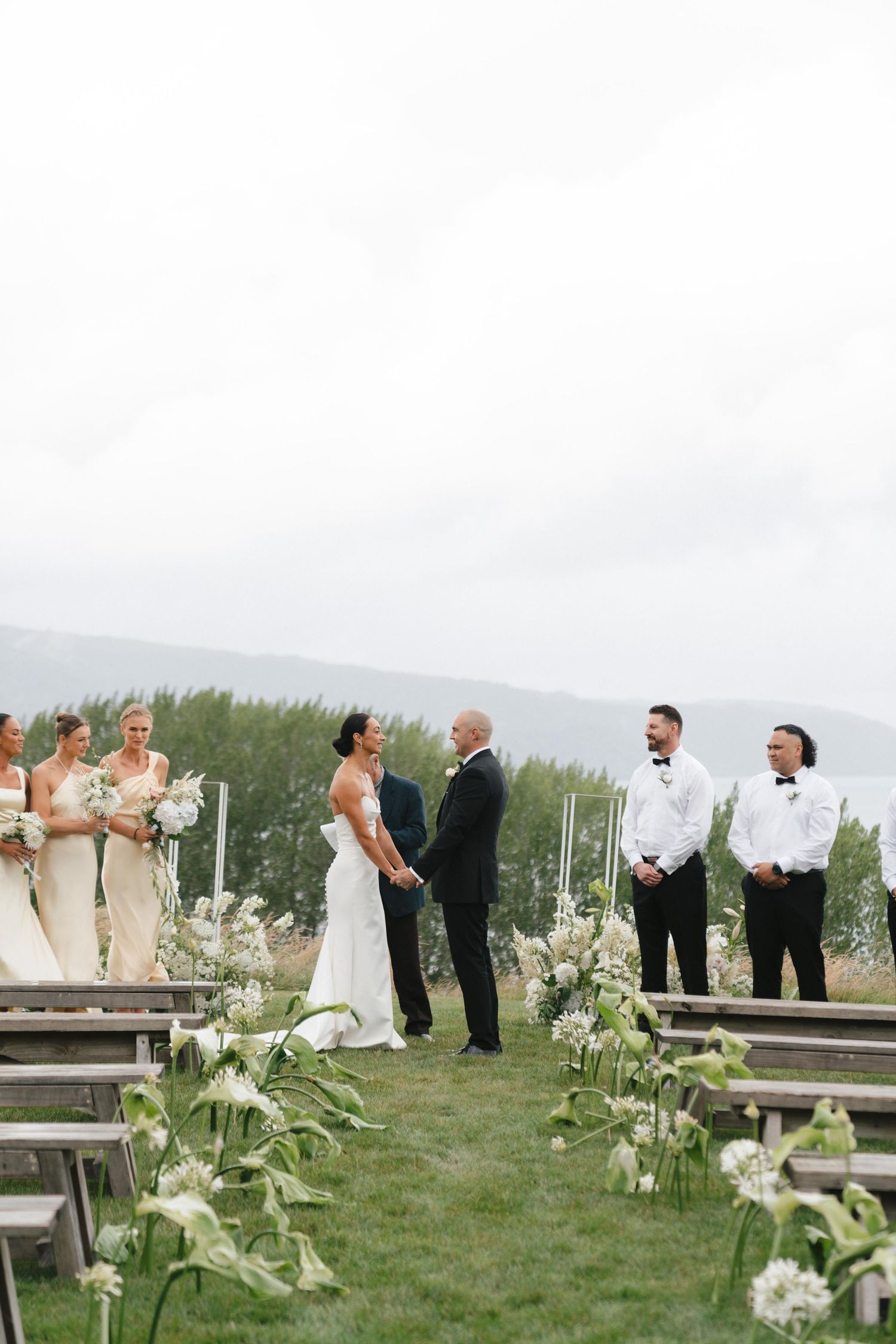 Outdoor mountain wedding ceremony with white floral aisle decorations and rustic wooden benches.