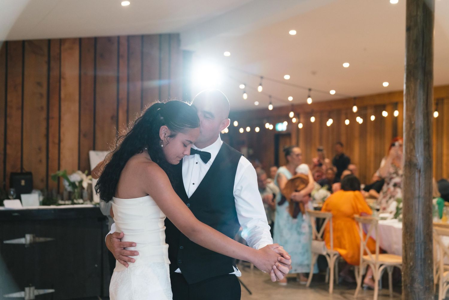Couple sharing their first dance in a dimly lit reception venue with string lights overhead.