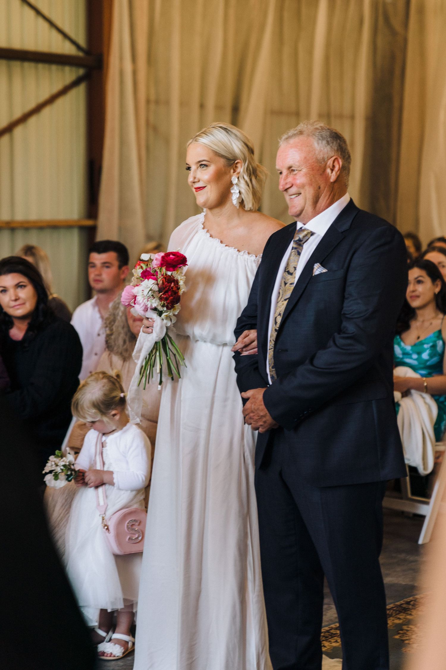 Wedding ceremony processional in a refined indoor venue with white and floral decor.