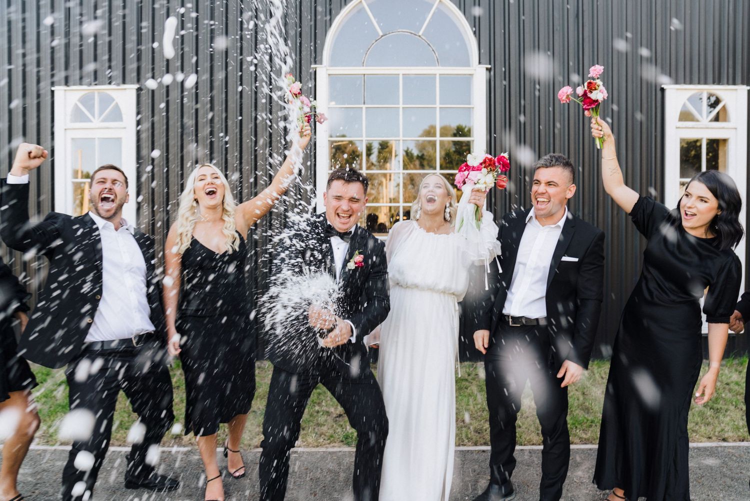 Wedding guests celebrate with a playful water splash moment outside on a sunny day.