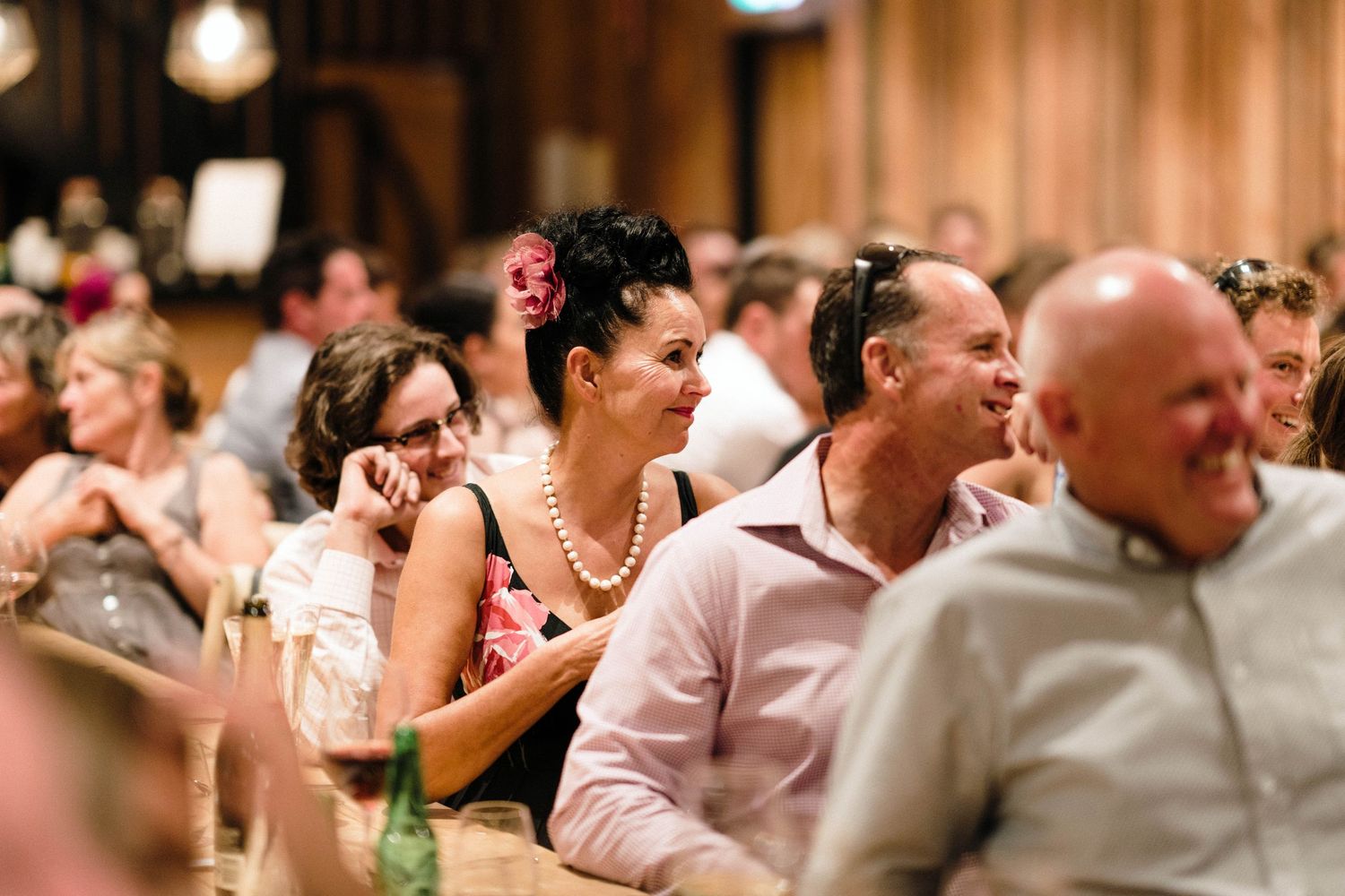 Wedding guests enjoying dinner and conversation at tables in a rustic wooden venue.