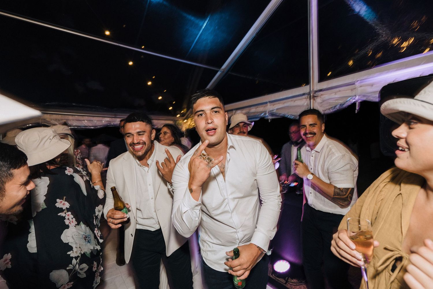 Wedding guests dancing and celebrating at night under tent lighting during reception.