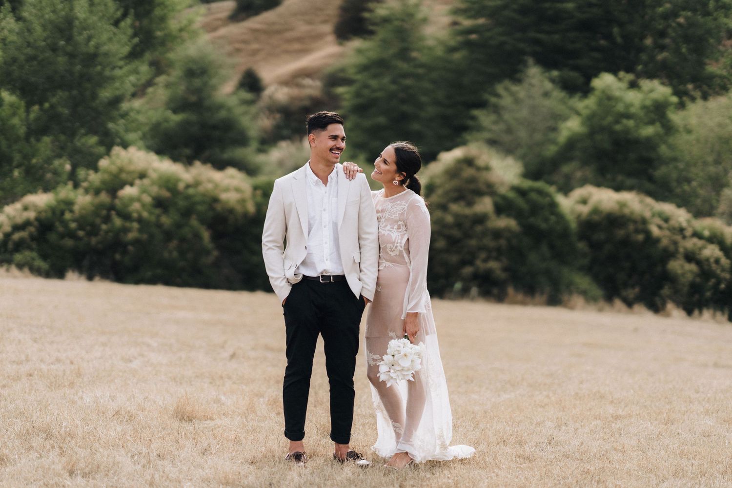 Wedding party strolling through a grassy field at sunset with mountains in background.