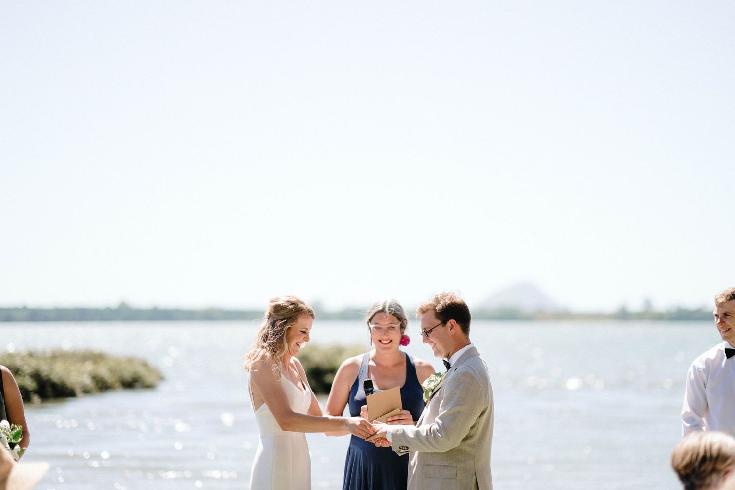 Intimate waterfront wedding ceremony with attendees gathered under bright blue skies.
