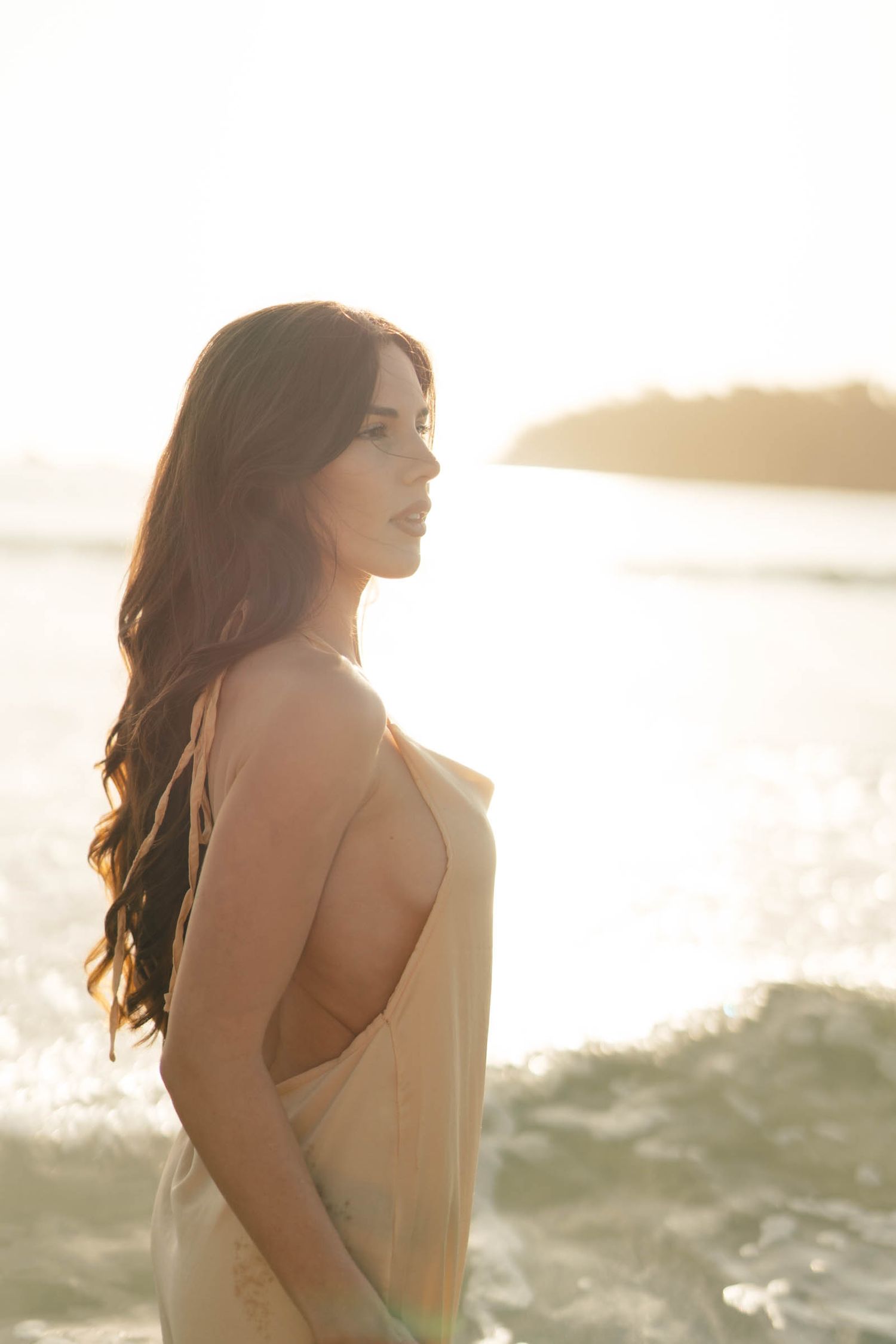 Side profile portrait against golden ocean sunset wearing flowing dress.