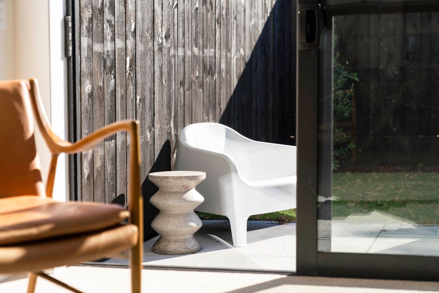 Mid-century modern furniture and white sculptural pieces in a sunlit corner by glass doors.