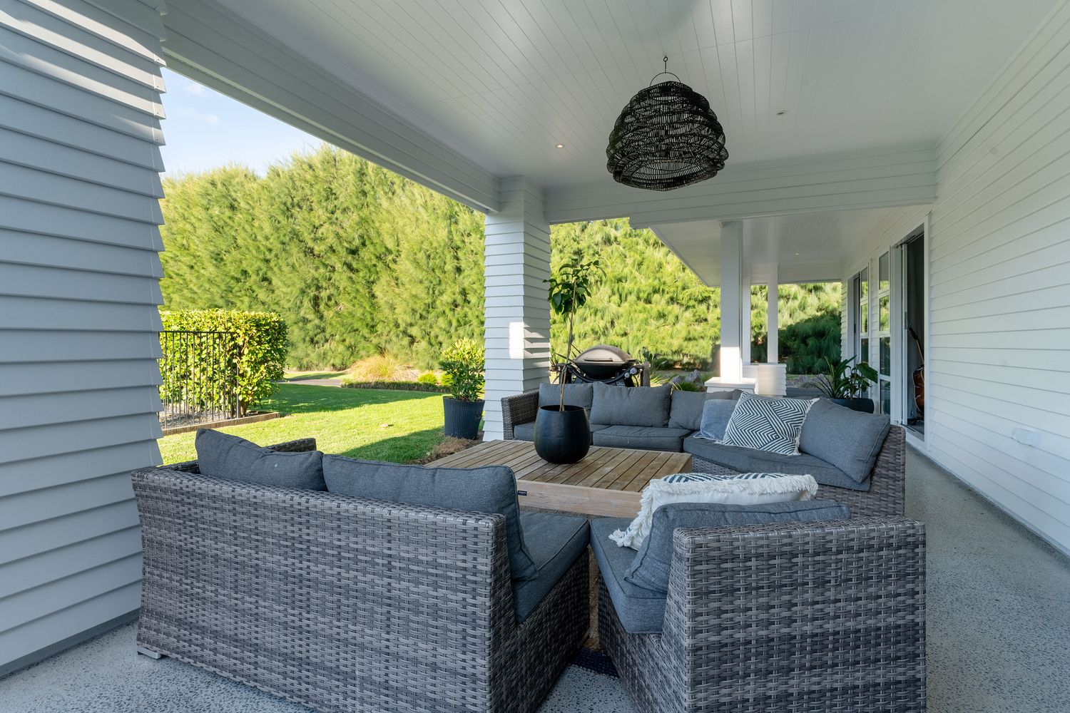 Luxurious covered patio with grey wicker outdoor furniture and plush cushions overlooking a landscaped backyard.