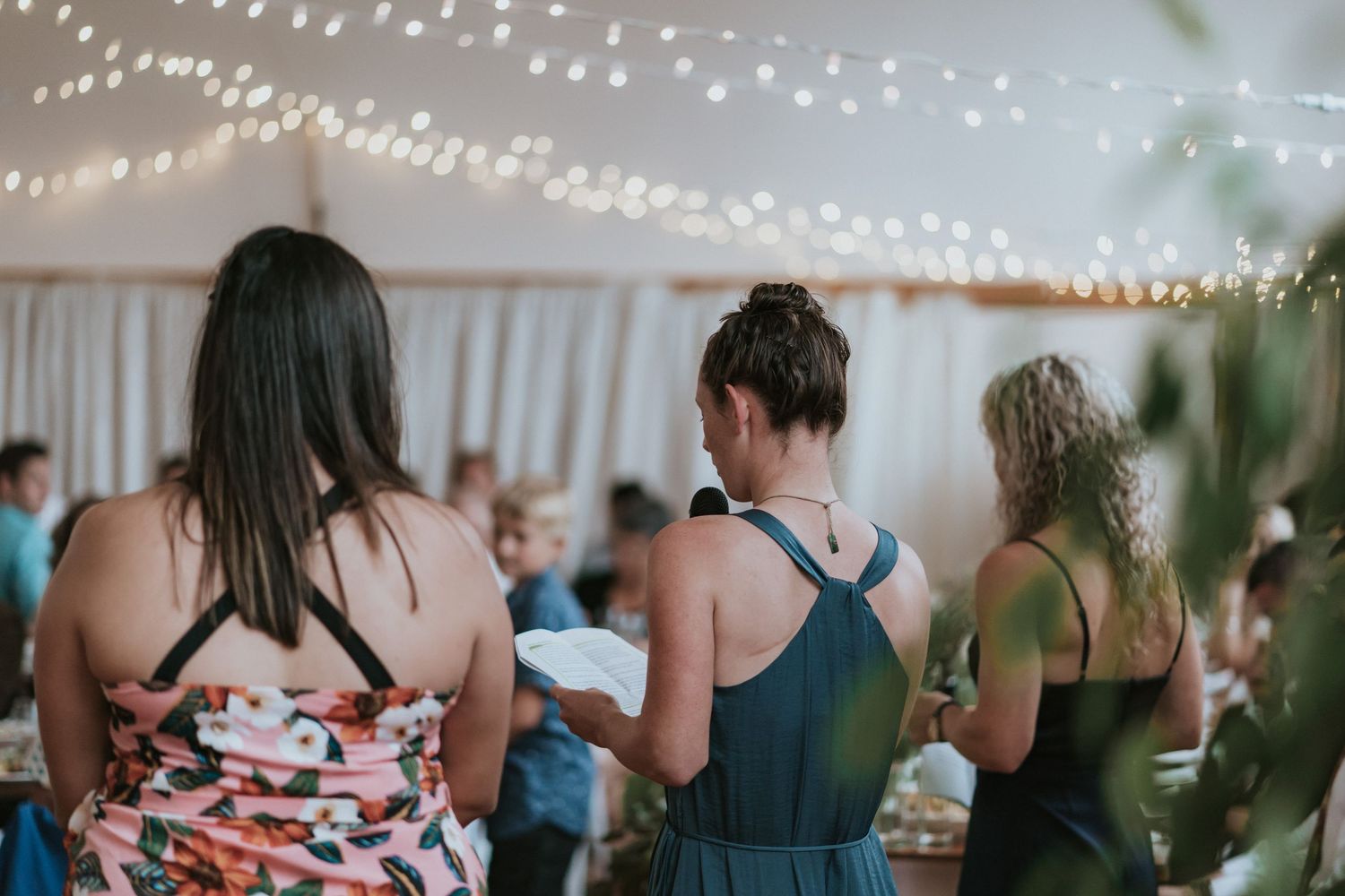 String lights illuminate a festive party scene with guests mingling and dancing in an indoor venue.