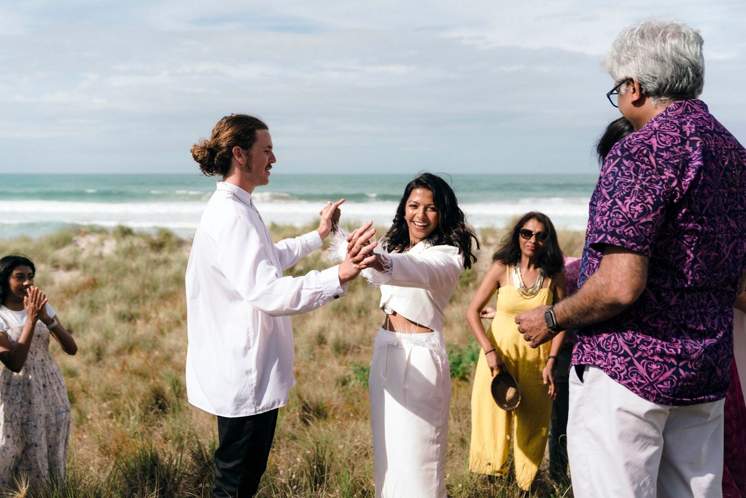 A couple celebrating their wedding ceremony on a scenic beach overlook with guests in attendance.